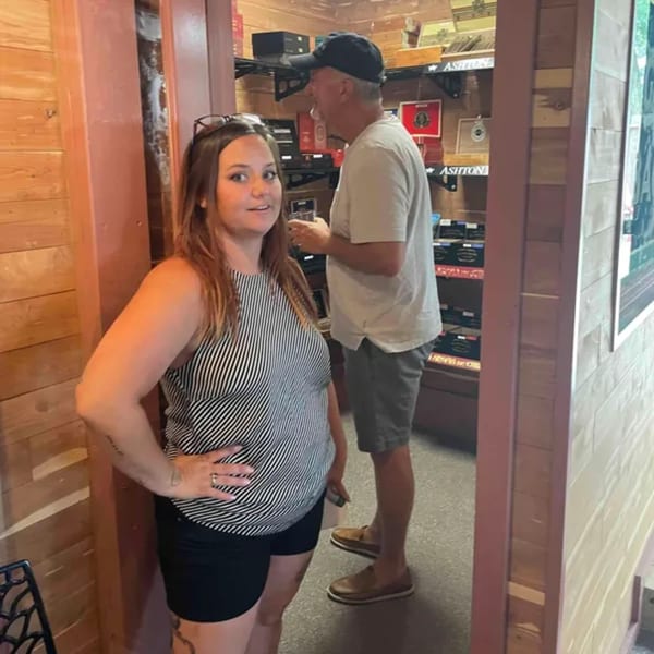 A woman in a striped top stands in a doorway, with a man in a cap behind her in Mo’s Cigar Bar.