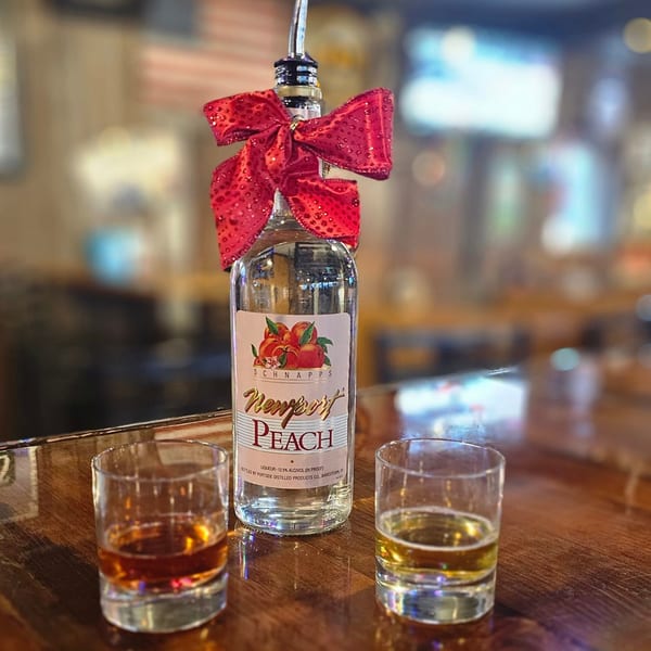 Newport Peach Schnapps bottle with a red bow and two glasses of amber liquid on a bar.