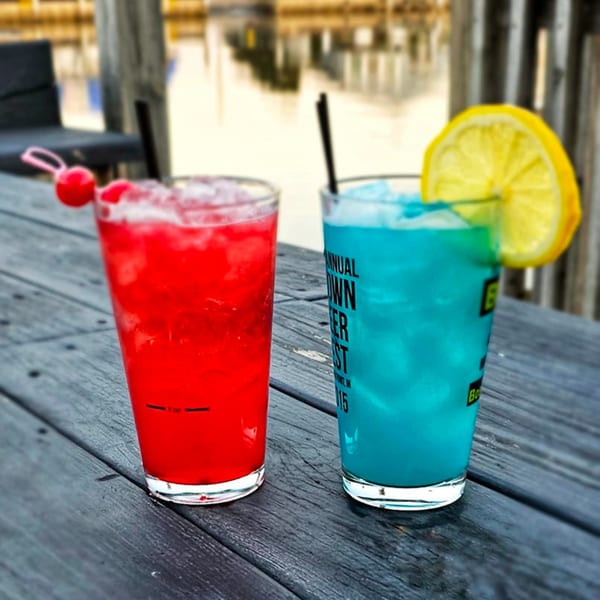 Two colorful cocktails, one red with a cherry and one blue with a lemon, on a wooden table.