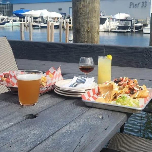 Nachos, fries, beer, and cocktails on a picnic table overlooking boats at Pier 33.