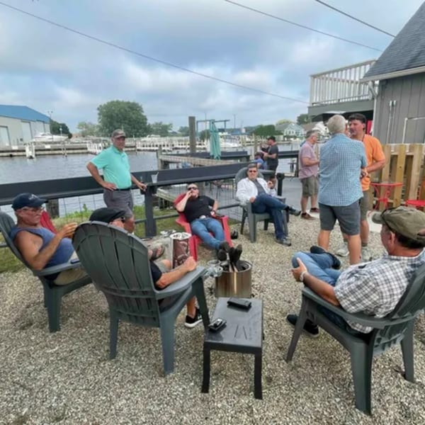 Men relaxing in chairs on a gravel patio overlooking a marina at On the River Tavern.