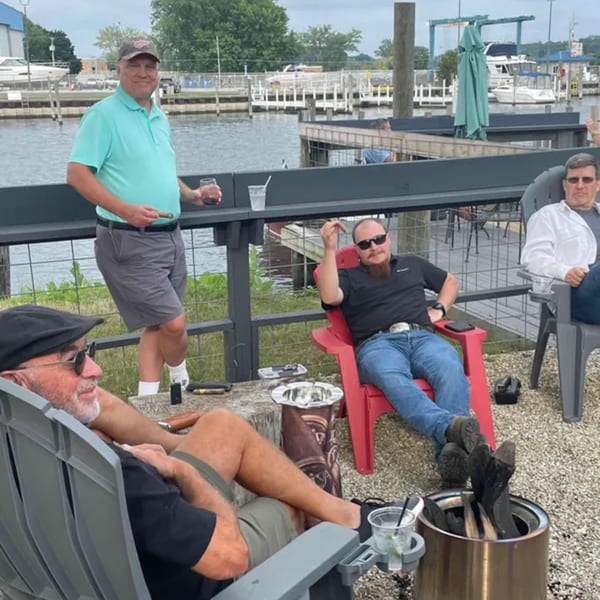 Four men relaxing outdoors by the water, enjoying cigars and drinks at Mo's Cigar Bar.