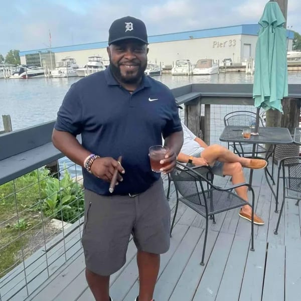 Man on a deck overlooking a marina, holding a cigar and a drink at On the River Tavern.
