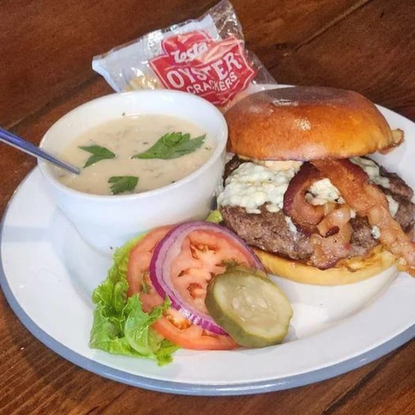 A bacon blue cheese burger with a side of clam chowder, oyster crackers, and salad.