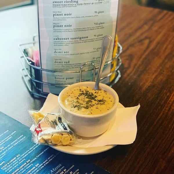 A bowl of creamy soup with crackers and a menu on a wooden table at On the River Tavern.