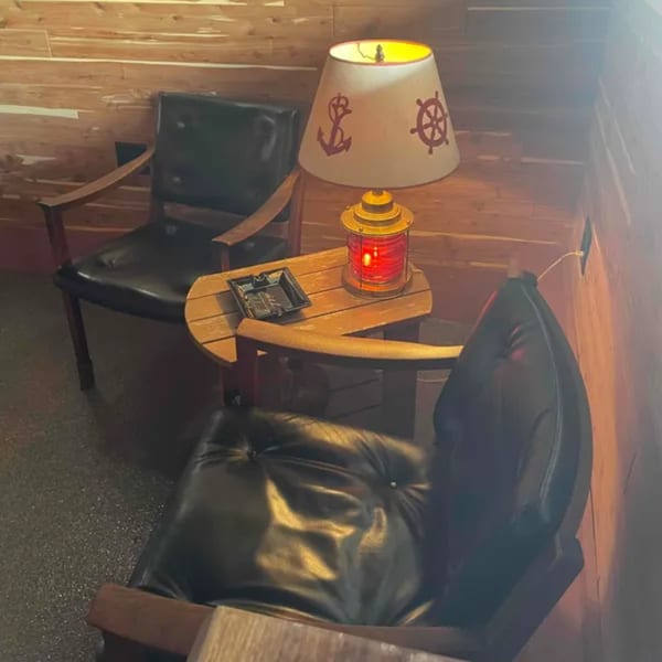 Two black leather chairs flank a small wooden table with a nautical-themed lamp and ashtray.