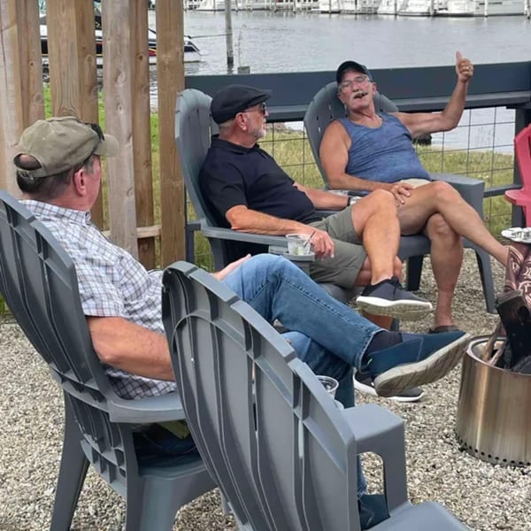 Three men relaxing in chairs on a patio overlooking a body of water with boats.