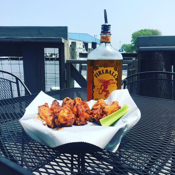 Spicy chicken wings and Fireball whiskey bottle on a metal table overlooking a marina.