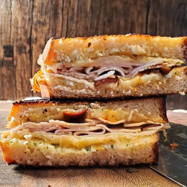 Two halves of a grilled turkey and cheese sandwich, stacked on a wooden surface.