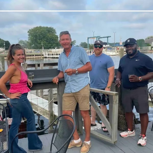 Four smiling patrons on a waterfront deck at On the River Tavern & Mo’s Cigar Bar.