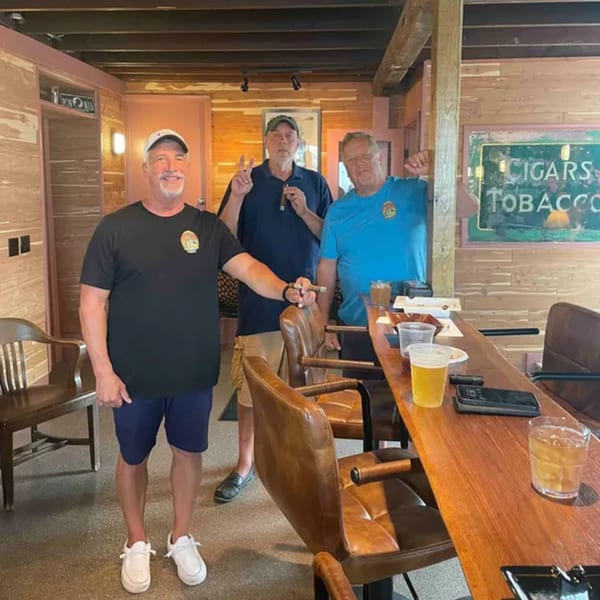 Three men enjoying cigars and drinks at the bar of Mo's Cigar Bar, with a "Cigars Tobacco" sign.